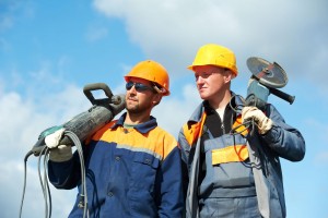 Two Builder workers with pneumatic hammer and grinding machine equipment over blue sky